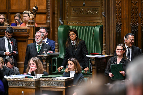 A group of 6-7 people including a woman in a large green chair respond with varying looks on their faces