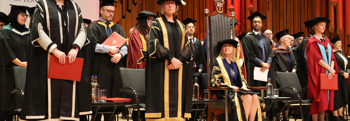 Graduation ceremony, faculty stand on stage and the Lady Mayor sits 