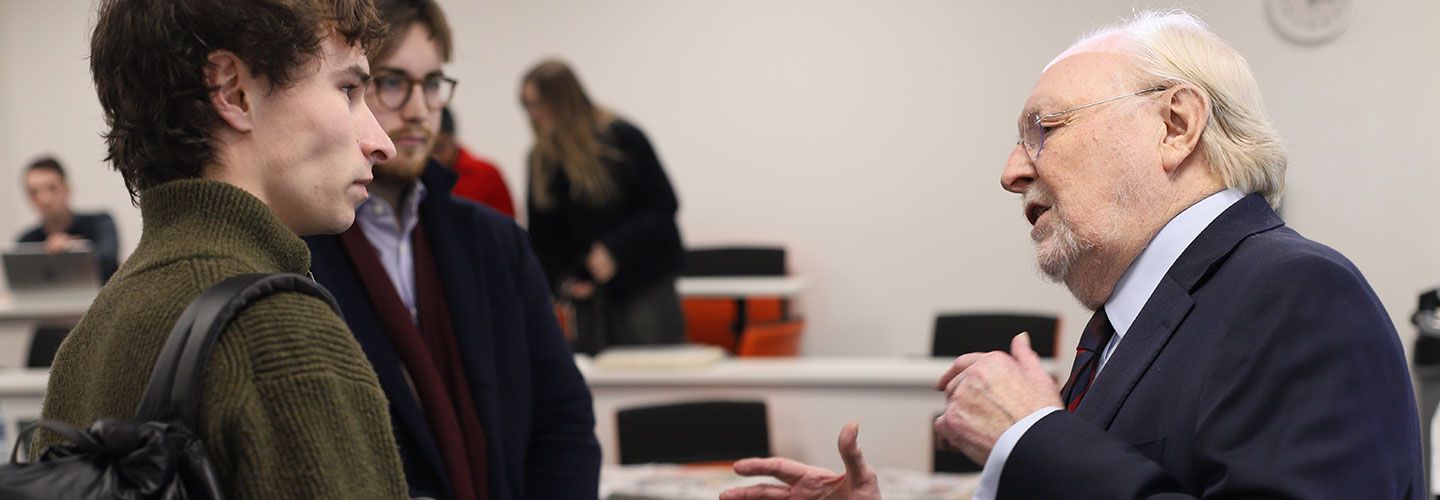 Lord Kinnock stands and talks to two students