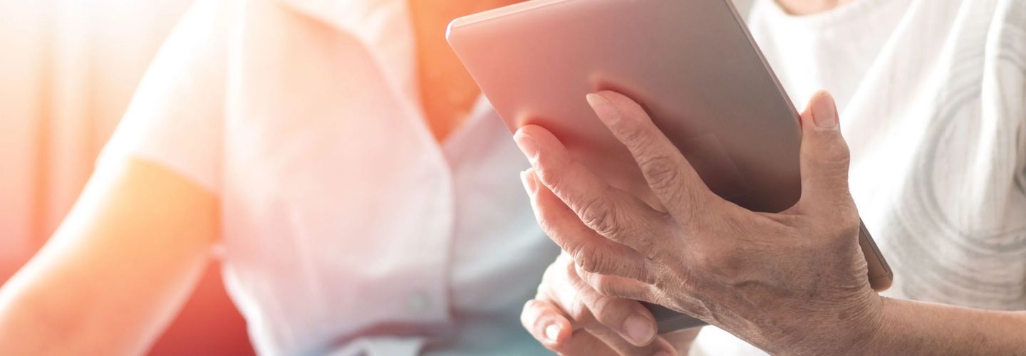 Older hands hold and use a tablet