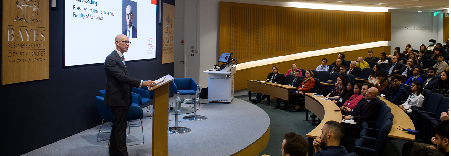 A well-dressed man stands at a lectern 