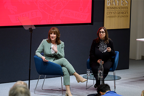 Two women in seats on a stage look at an unseen questioner speaking from the side 