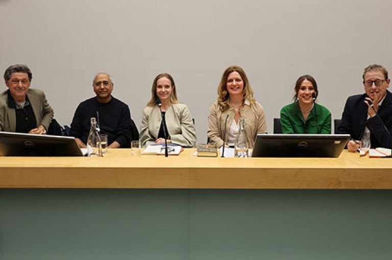 The speakers sit in a row and smile to camera