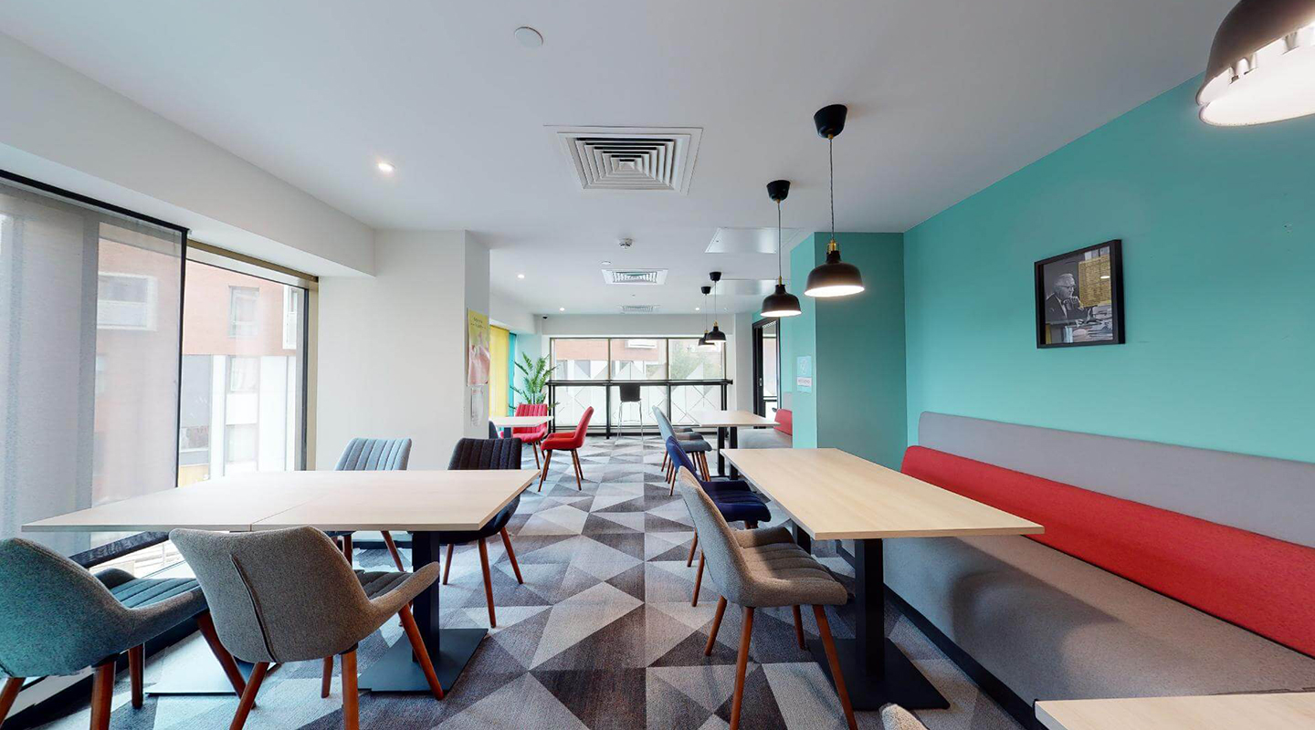 Bright communal study space with large tables and chairs, and floor to ceiling windows.