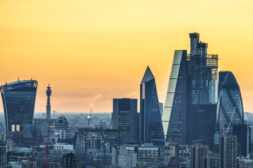 Grey buildings of the City of London sit against a yellow and orange sky. Buildings include Cheese Grater, Gherkin and Walkie Talkie amongst many others.