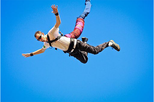 A bunjee jumper has their arms stretched out as they fall while attached to a thick colourful rope