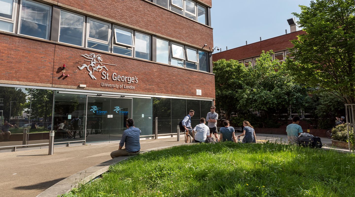Students sitting and chatting outside on a sunny day, in front of the entrance to St George's, University of London (Tooting campus).