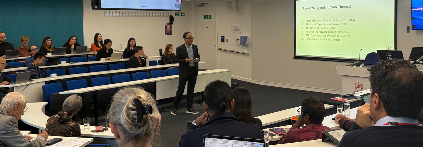 A man stands in front of a screen talking to around 30 people in a lecture theatre