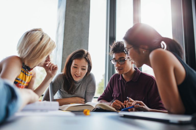 A group of students smile and look down at books together