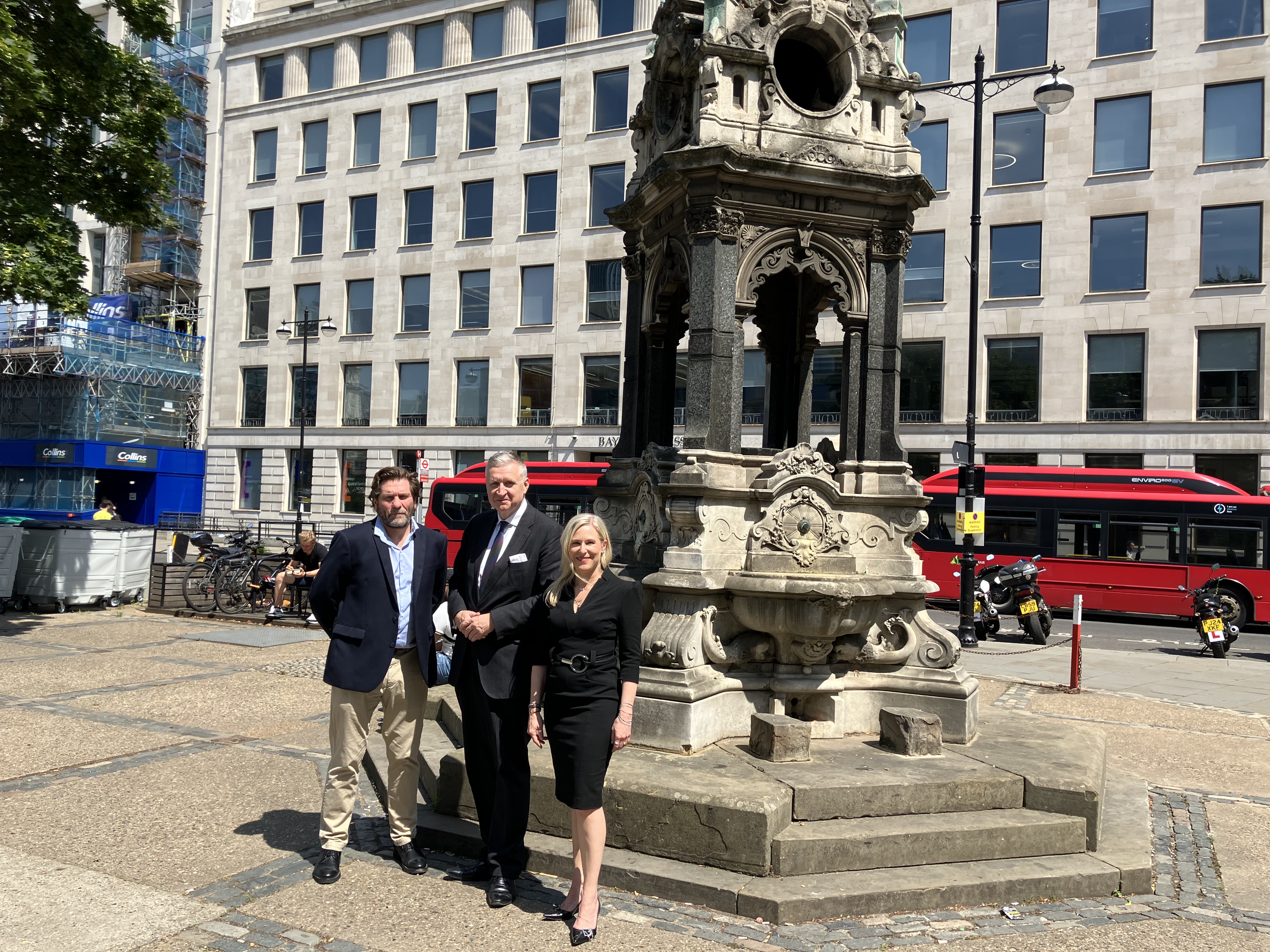 Two men and a woman stand in front of an elaborate drinking fountain