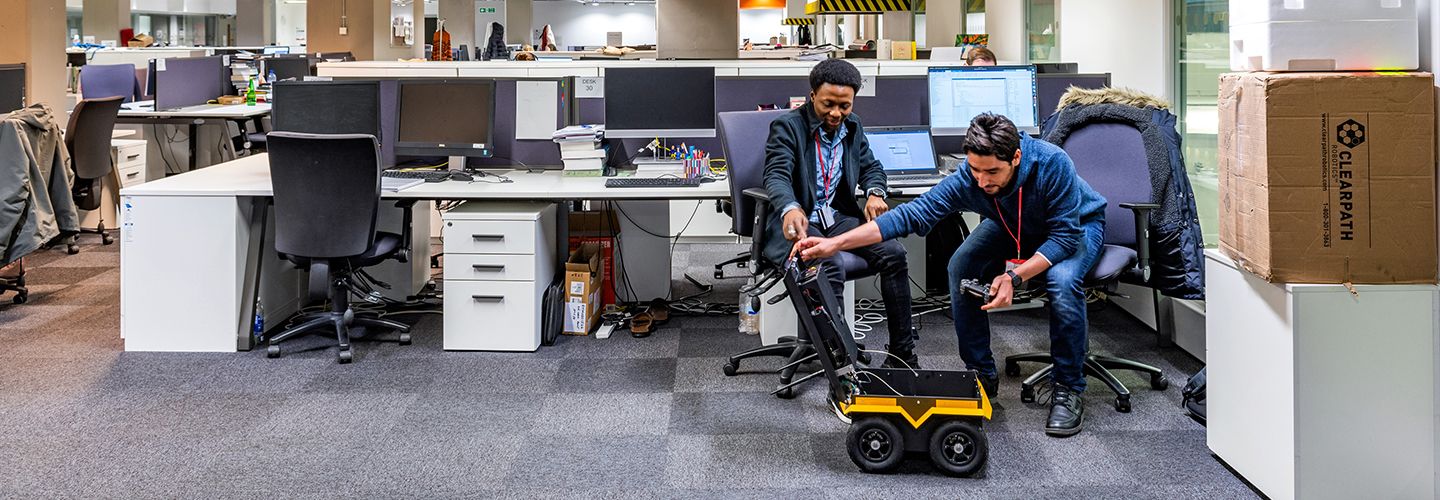 PhD students in an office looking inside Jackal robot