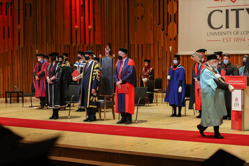 The academic procession wear face coverings on stage.