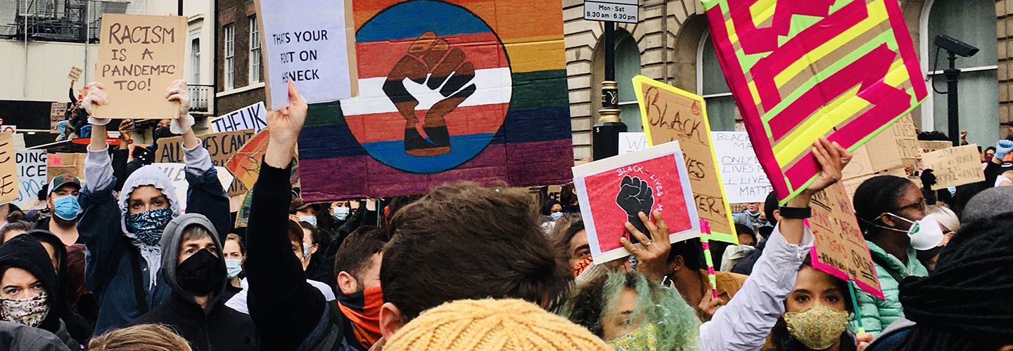 People wearing face masks and waving colourful homemade banners and signs on a Black Lives Matter protest march during the Covid-19 pandemic. One sign says 