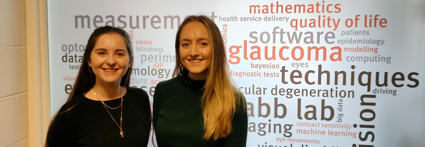 Josie Evans and Dr Bethany Higgins standing outside the Crabb Lab.  The large window of the Crabb Lab has a word cloud on it with all the words that relate to what the Crabb lab does