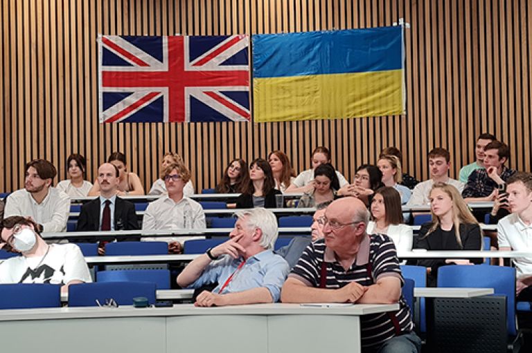 Audience of students and staff with Union Jack and Ukraine flags on the wall.