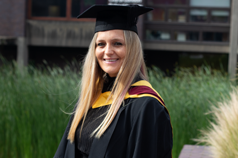 A woman wearing a graduation cap smiles outside