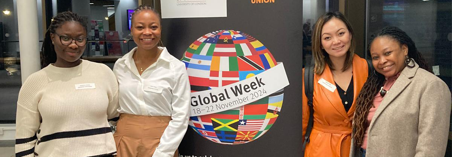 Four women stand next to a Global Week Banner