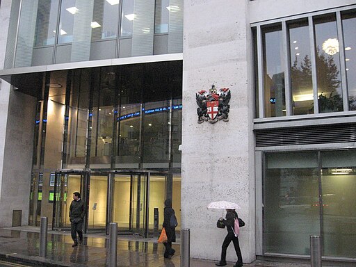 Two men are walking separately out of the London Stock Exchange building which has a large Corporation of London logo