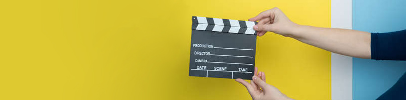 Female hands holding film clapperboard on yellow background