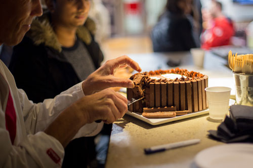 Obscured party guests cut a lice of decadent chocolate cake.