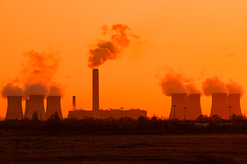 Coal station cooling towers with smoke coming out the chimney into orange sky