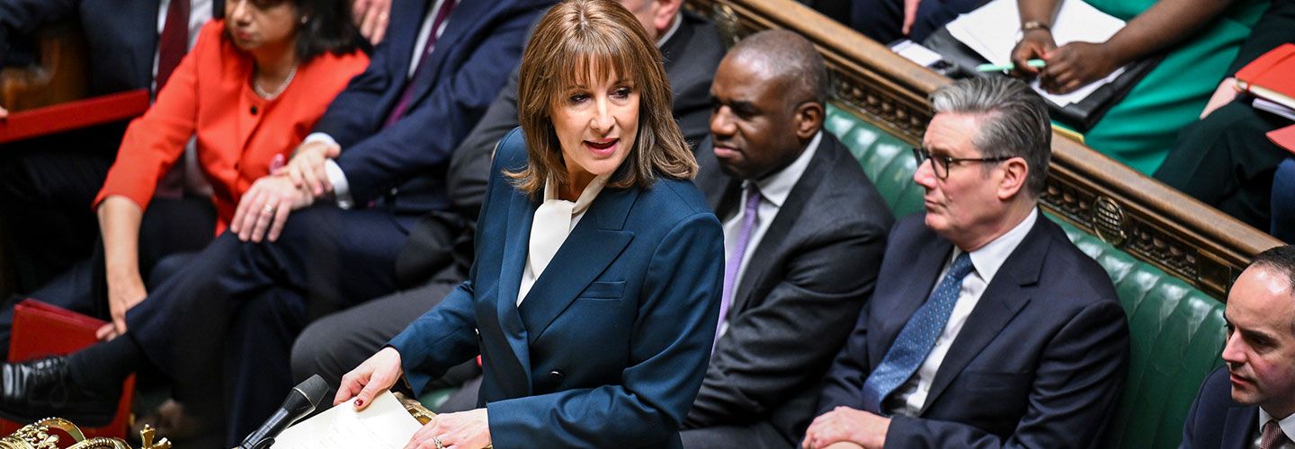 An image from above of Chancellor Reeves standing at a lectern and reading her Autumn Budget statement in the House of Commons. Behind her sit Prime Minister Keir Starmer and front benchers.