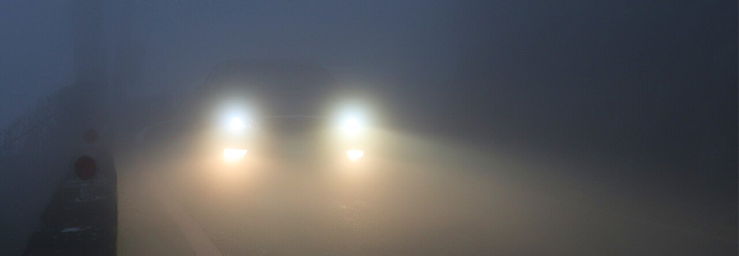 A car's lights shine out through the fog