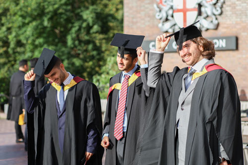Three graduates practise doffing their caps. 