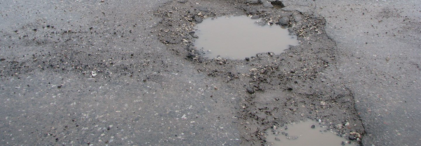 An image of two huge potholes in a road, which are filled with dirty water.