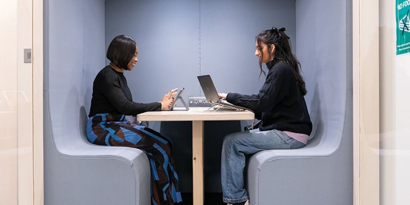 Two students sat at table facing each other in library pod