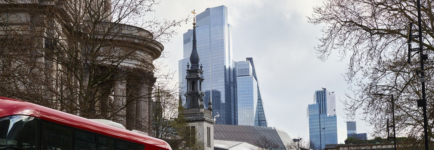 London landscape with the top of a red bus and the Bank on England in the foreground and City's business district skyscrapers in the background.