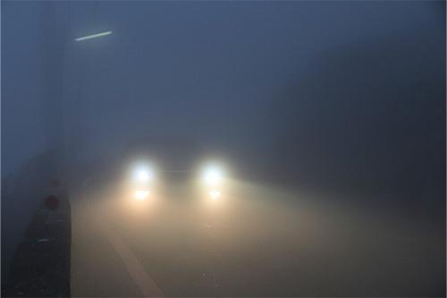 A car's lights shine out through the fog