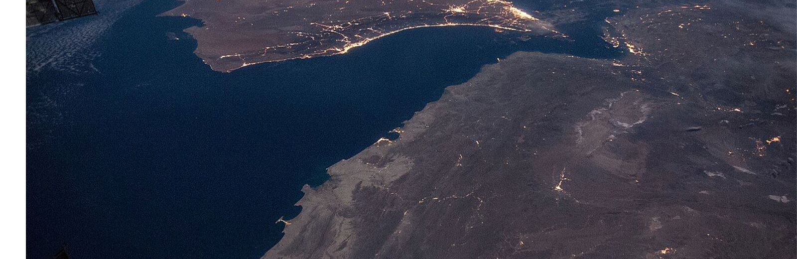 A few lights are visible in the darkness with the faint outline of land against the sea