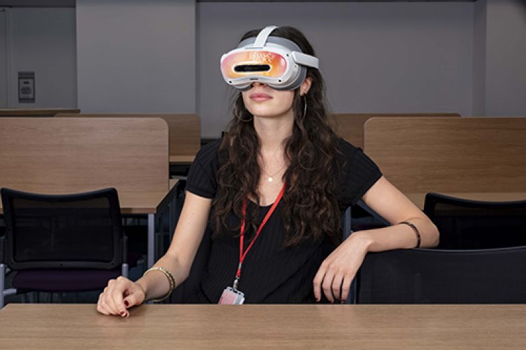 A woman wearing a white virtual reality headset with 'phase space' branding sits at a wooden desk in a classroom setting.