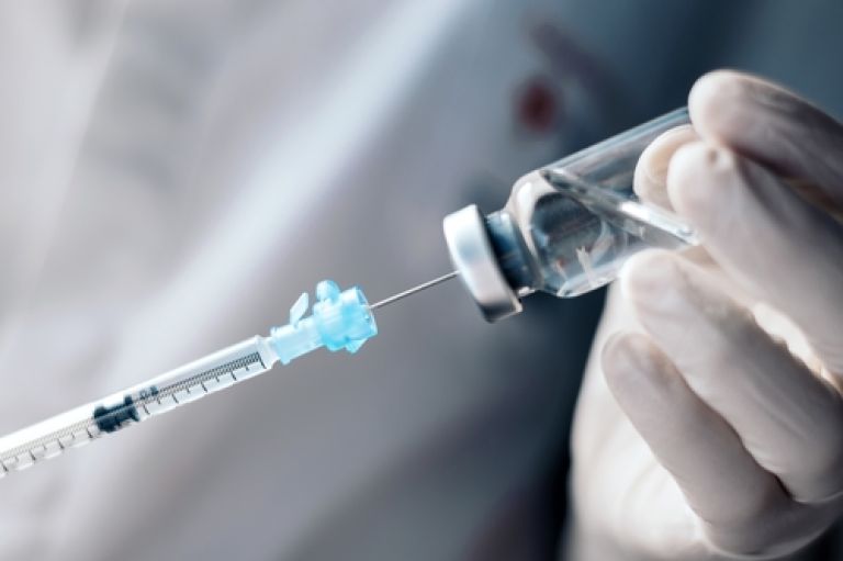 Injection being prepared from glass vail, held by blue gloved hands