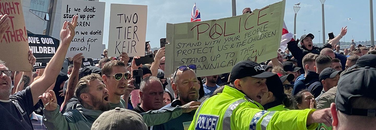 An image of a group of men shouting and protesting. They hold signs that read 