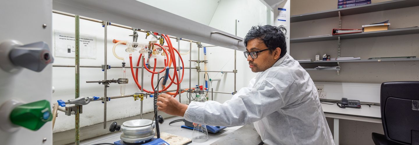 Male student in white lab coat troubleshooting cables in the Optic Sensor Lab.