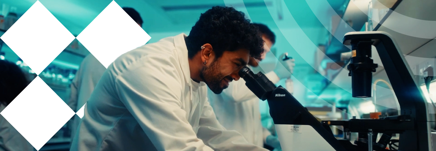 A man in a lab coat examines a microscope, focused on his research in a laboratory setting.