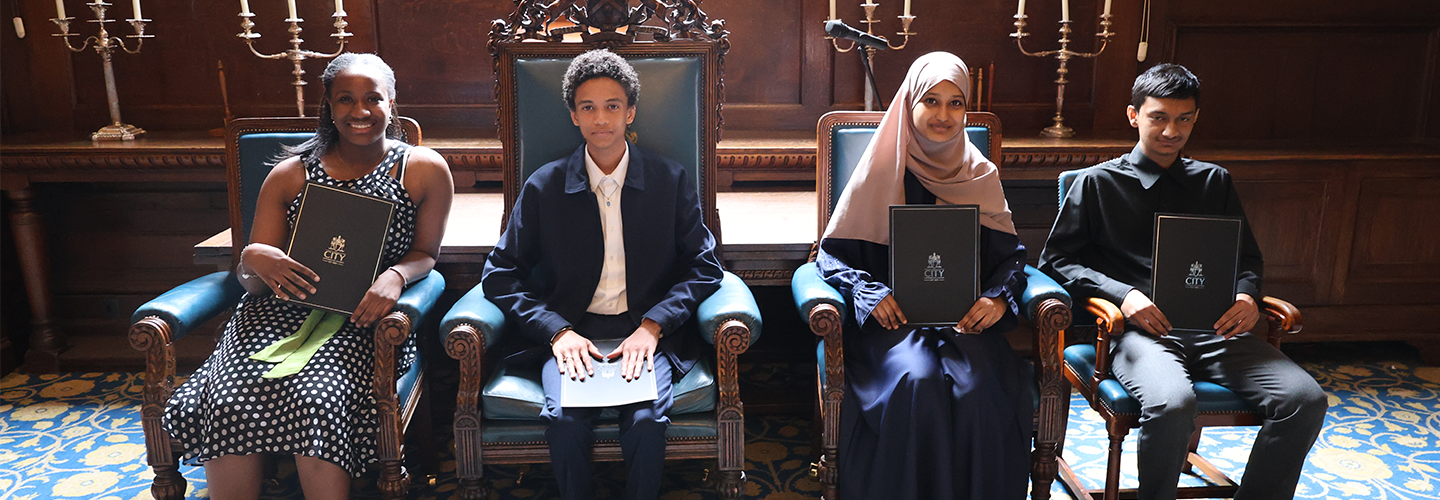 Pupils sit on chairs holding their summer school certificates