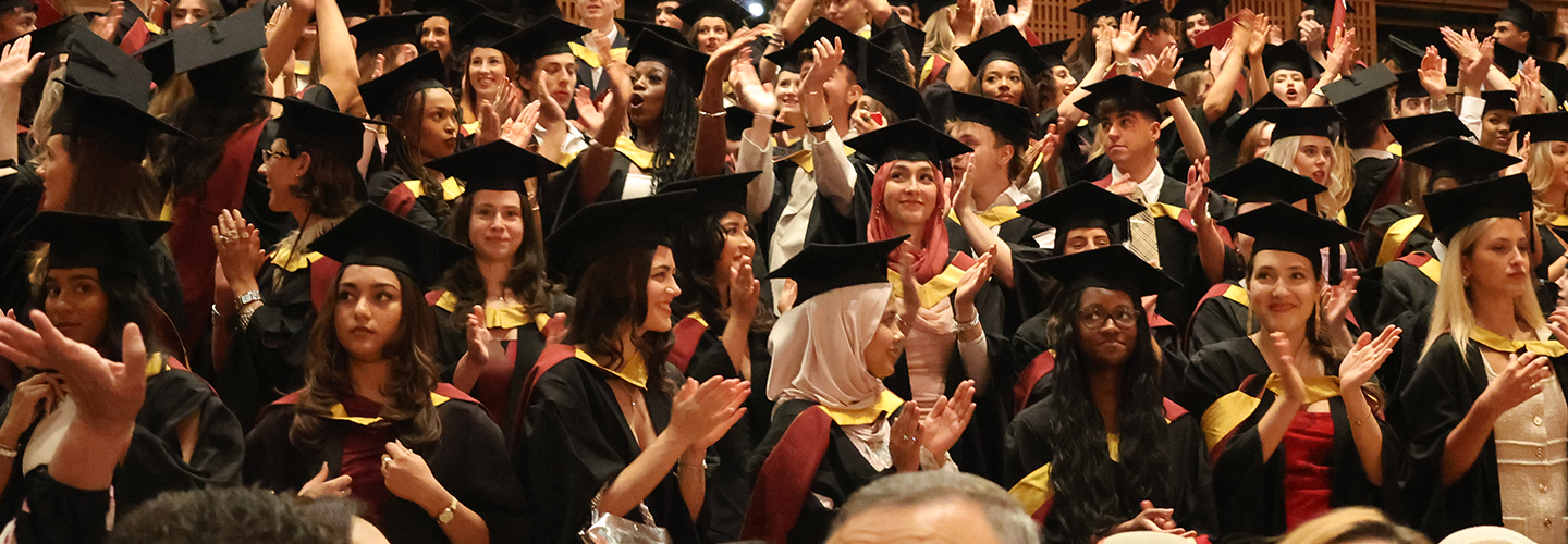 Graduates in caps and gowns stand and cheer in a theatre audience