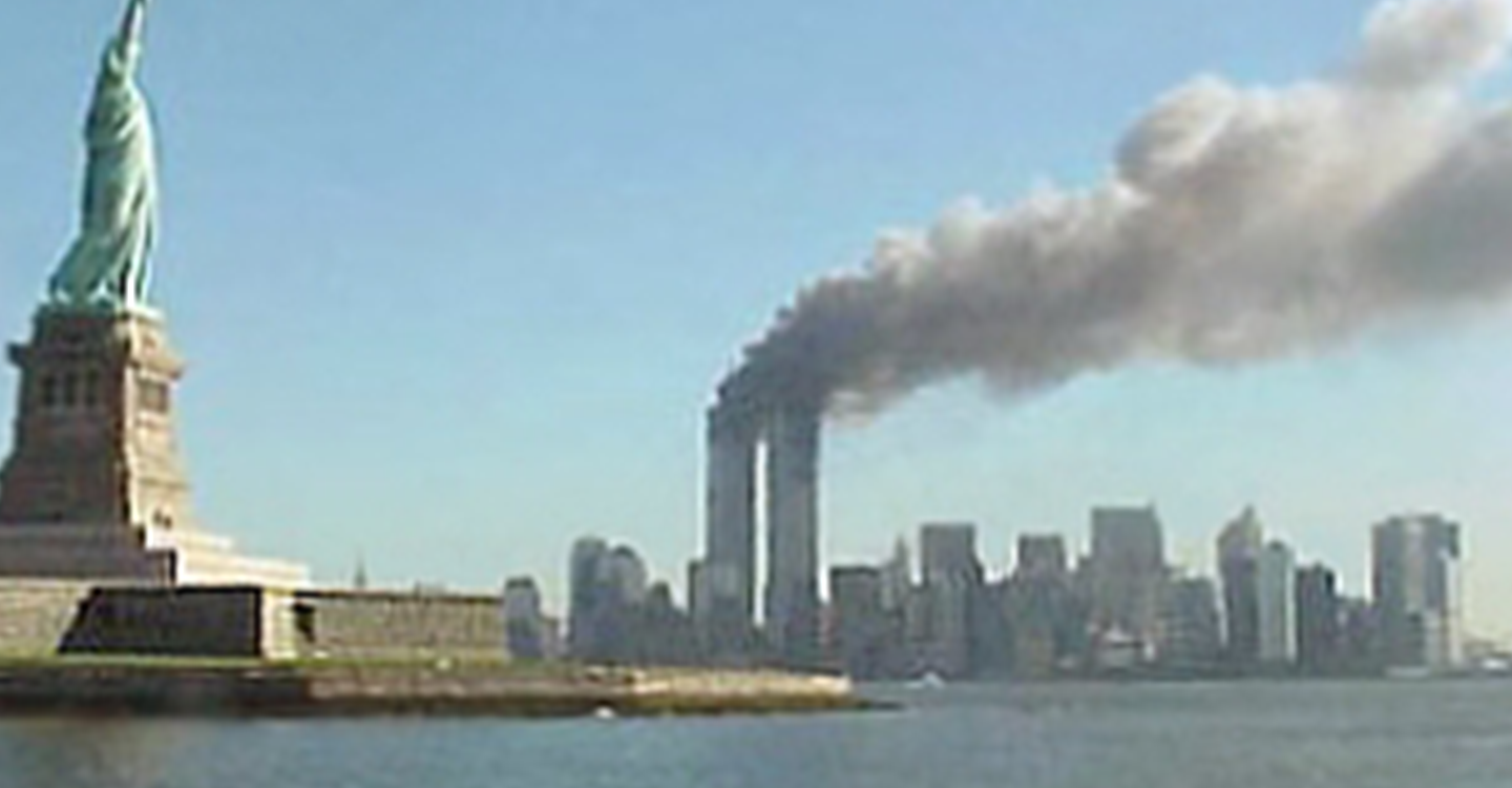 The Statue of Liberty is in the foreground with smoke billowing from the Twin Towers